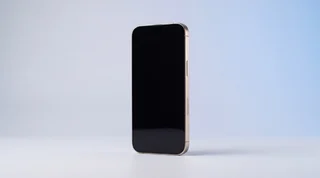 A single iPhone 15 Pro lying flat on a clean pale-grey studio surface with its screen dark, an unfinished arc of blue light curving around it on the background like a countdown