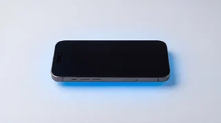 A pristine iPhone standing upright with a soft blue motion streak behind it on a clean studio surface