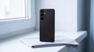 A black Samsung Galaxy S25 lying face down on a pale-grey surface with a white USB-C cable unplugged just in front of its charging port
