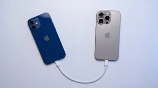 An older navy iPhone 12 and a newer titanium iPhone 16 Pro Max standing upright with a soft blue arc of light flowing between them, transferring data
