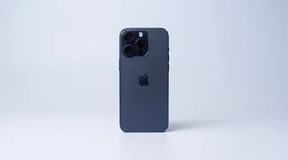 A modern iPhone covered in water droplets, lying in a small pool of water on a clean studio surface