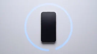 A single iPhone 15 Pro lying flat on a clean pale-grey studio surface with its screen dark, an unfinished arc of blue light curving around it on the background like a countdown