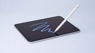 A single iPad Pro lying flat with an Apple Pencil drawing an unsteady wavy trail of blue light across its dark screen