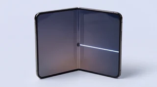 An iPhone Duo standing half open like a book on a pale grey studio surface, its inner folding screen showing the fault owners are reporting: a dark dead patch at the hinge, a thin line up the crease and a bright stripe of stuck pixels across the right half
