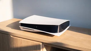 A PlayStation 5 lying flat on a pale oak media unit in warm summer sunlight, with clear space around it