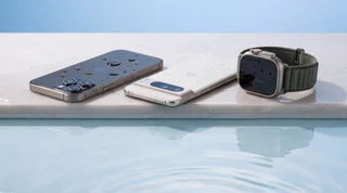A refurbished iPhone, Google Pixel and Apple Watch lined up on the wet edge of a pool with water droplets on their screens